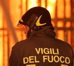 Vigile del fuoco a terra durante intervento antincendio in zona boschiva, colleghi intorno