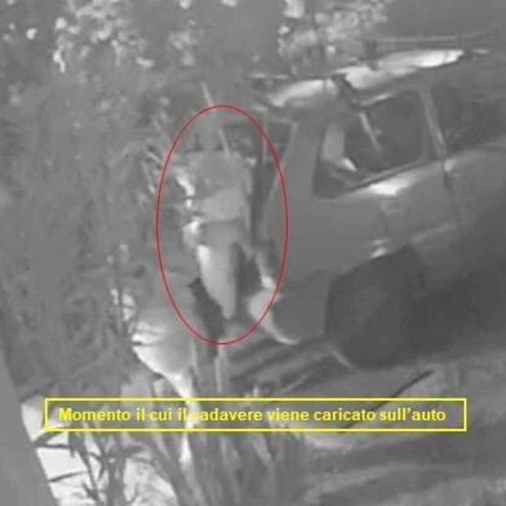 Le telecamere riprendono il momento in cui il cadavere avvolto in un lenzuolo viene carica...