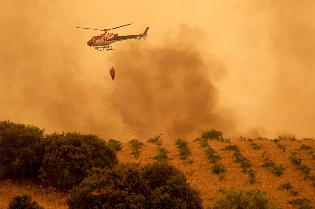 Persone evacuate su strade affollate, colonne di fumo visibili in cielo, vigili del fuoco al lavoro