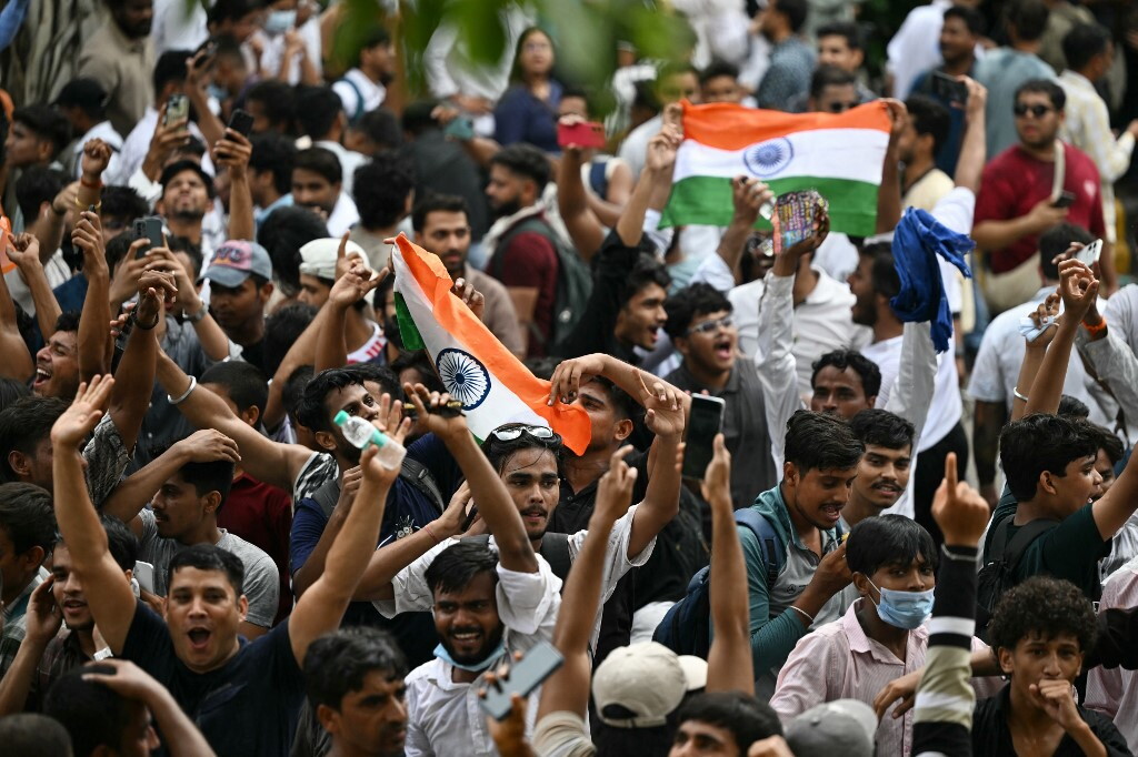 Piazza gremita a New Delhi con giovani manifestanti che protestano pacificamente brandendo cartelli, immagine di approfondimento