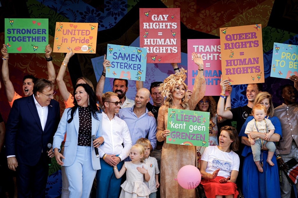 Regina e sindaca su palco ad Amsterdam con cartelli sui diritti umani durante cerimonia WorldPride